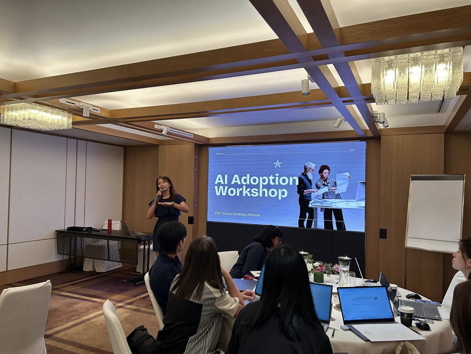 Photograph of Geargina Tan (Coach Gina), Singapore-based AI workshop facilitator and COO of WTFox.ai, presenting at the BNF Group strategy retreat, Ritz-Carlton Singapore, 30 March 2026. Real photo, attendees seen from behind. AI training for teams in Singapore.